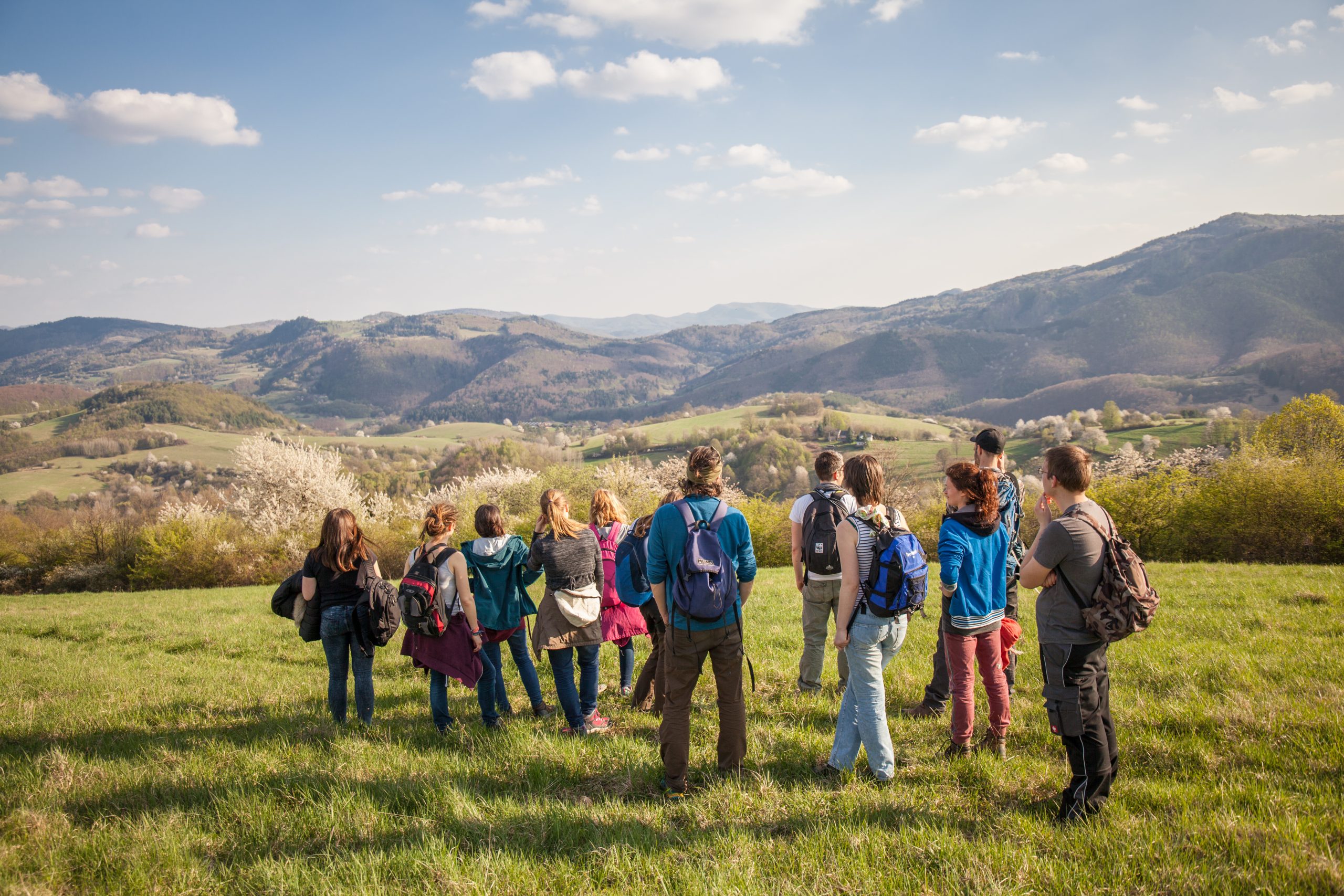 Eine Gruppe Jugendlicher stehen auf einer Wiese und schauen in ein entferntes Gebirge.