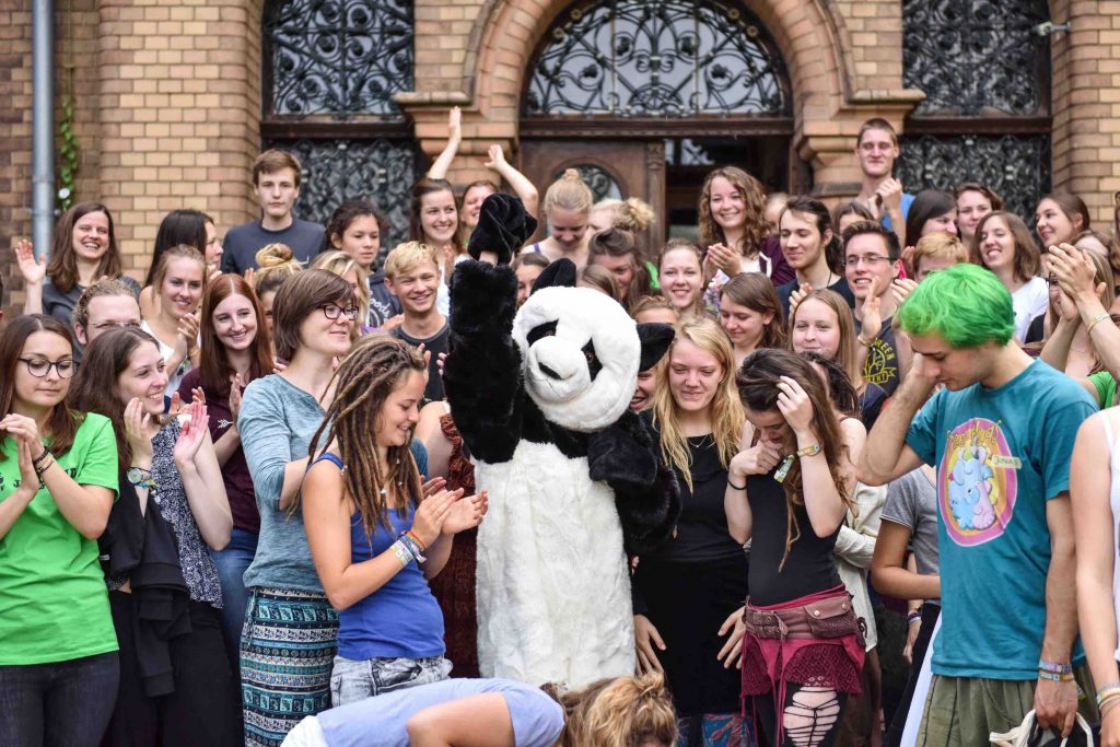 Ein Panda in der Mitte um den viele Jugendliche herum stehen