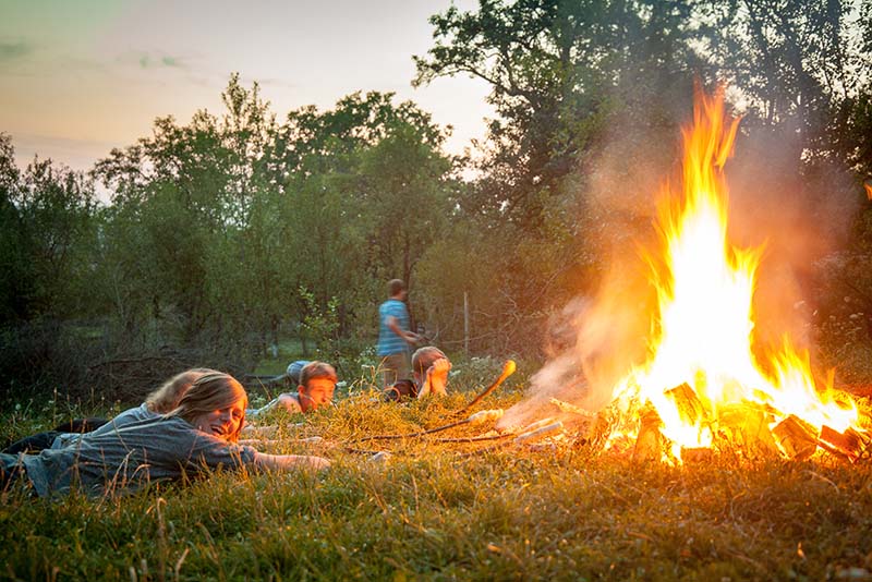 Jugendliche liegen im Gras und rösten an einem Stock Stockbrot über dem Feuer