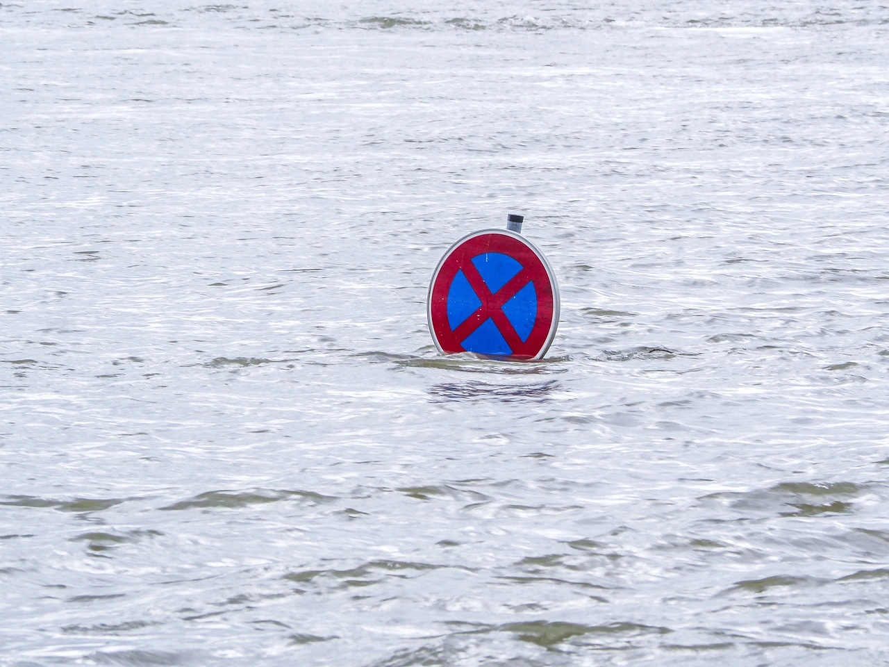 Das Foto zeigt eine überflutete Fläche. Es ist nur Wasser zu sehen, aus dem Wasser ragt ein Straßen-Verbots-Schild.