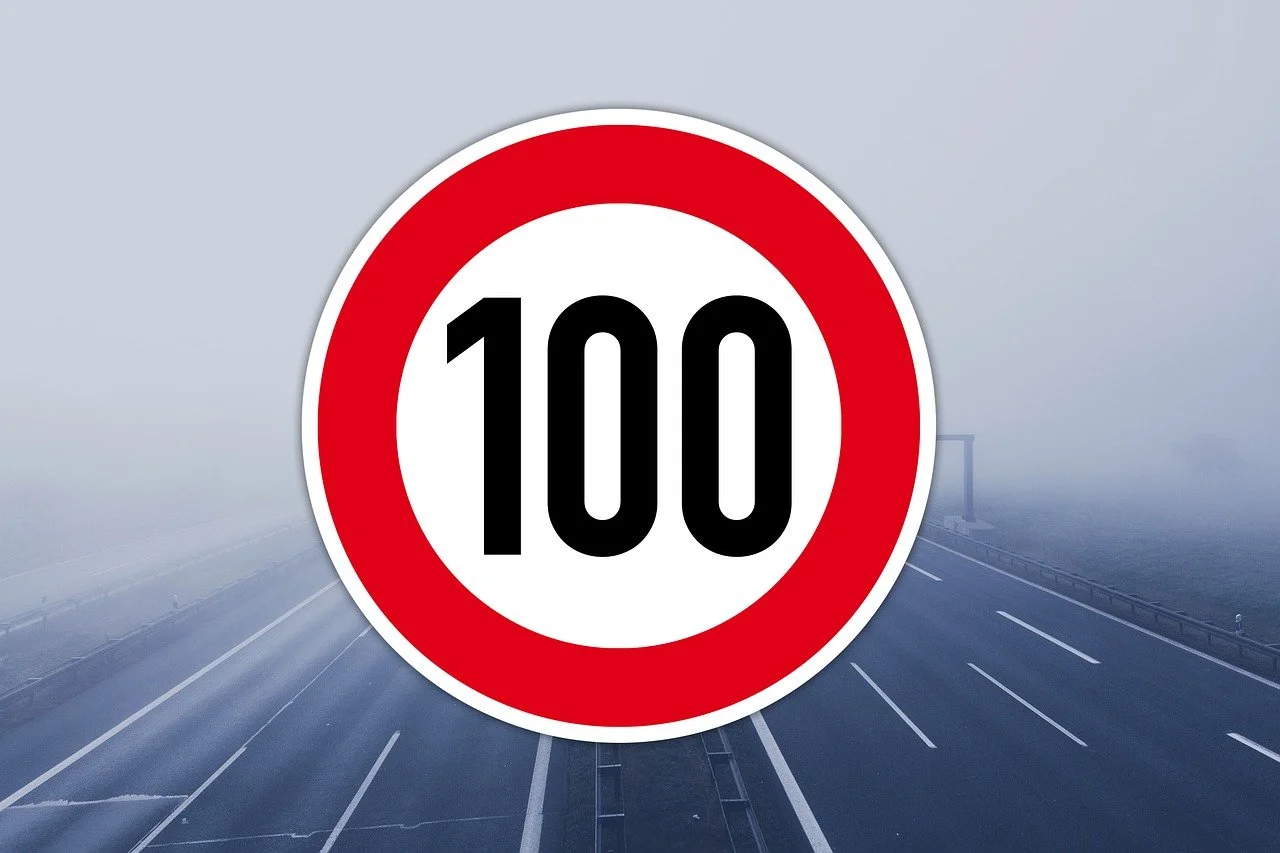 Das Foto zeigt ein Verkehrsschild mit der Geschwindkeitsbegrenzung auf 100 km/h. Im Hintergrund ist eine leere Autobahn.