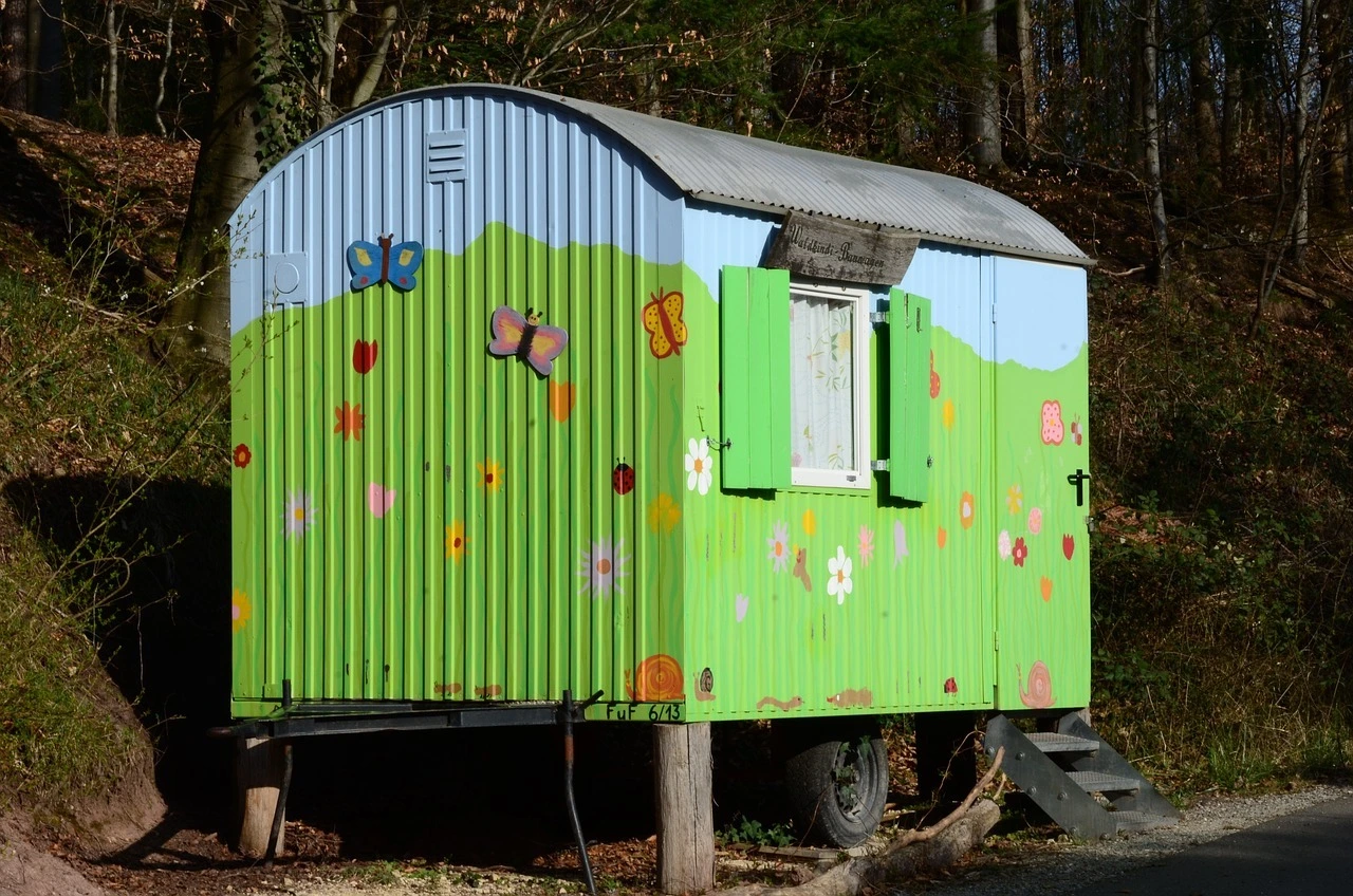 Das Foto zeigt einen Bauwagen. Er ist bunt angemalt mit einer Wiese und Schmetterlingen. Zum Eingang des Bauwagens führt eine kleine Treppe.