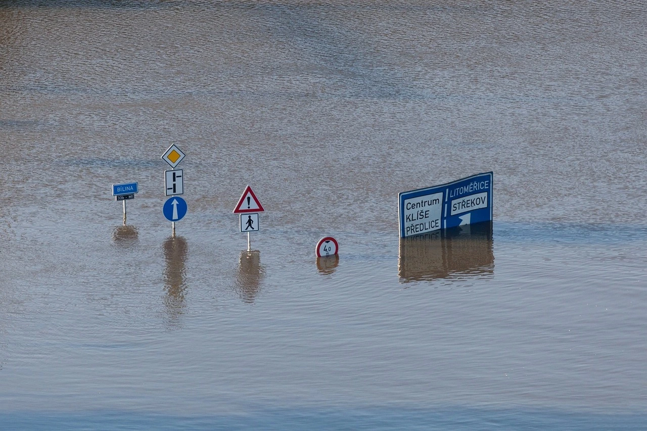 Das Foto zeigt eine überschwemmte Straße. Aus dem Wasser ragen mehrere Straßenschilder.