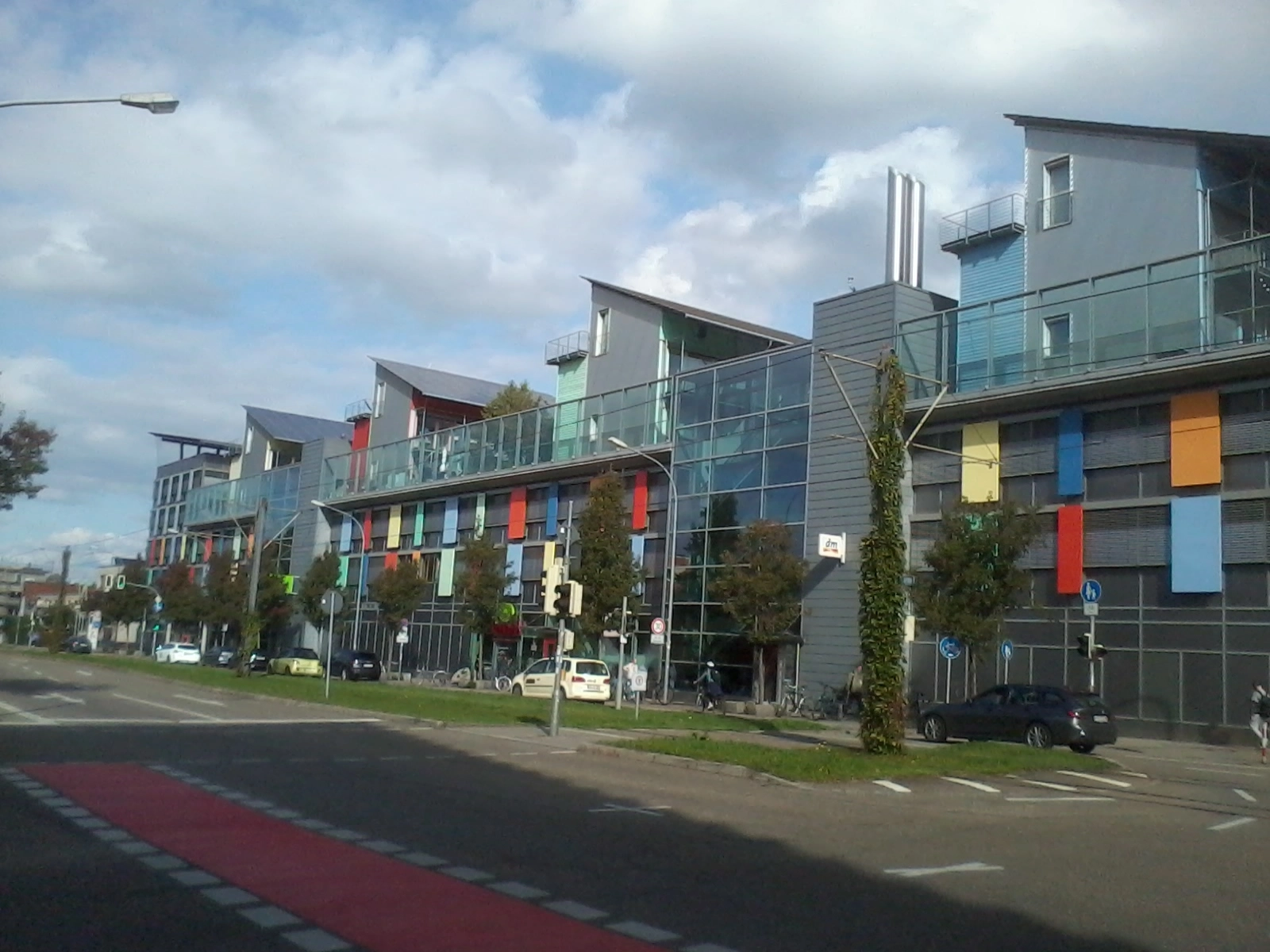 Das Foto zeigt ein buntes, großes Gebäude an einer Straße. Auf dem Dach sind Penthäuser und Solaranlagen.