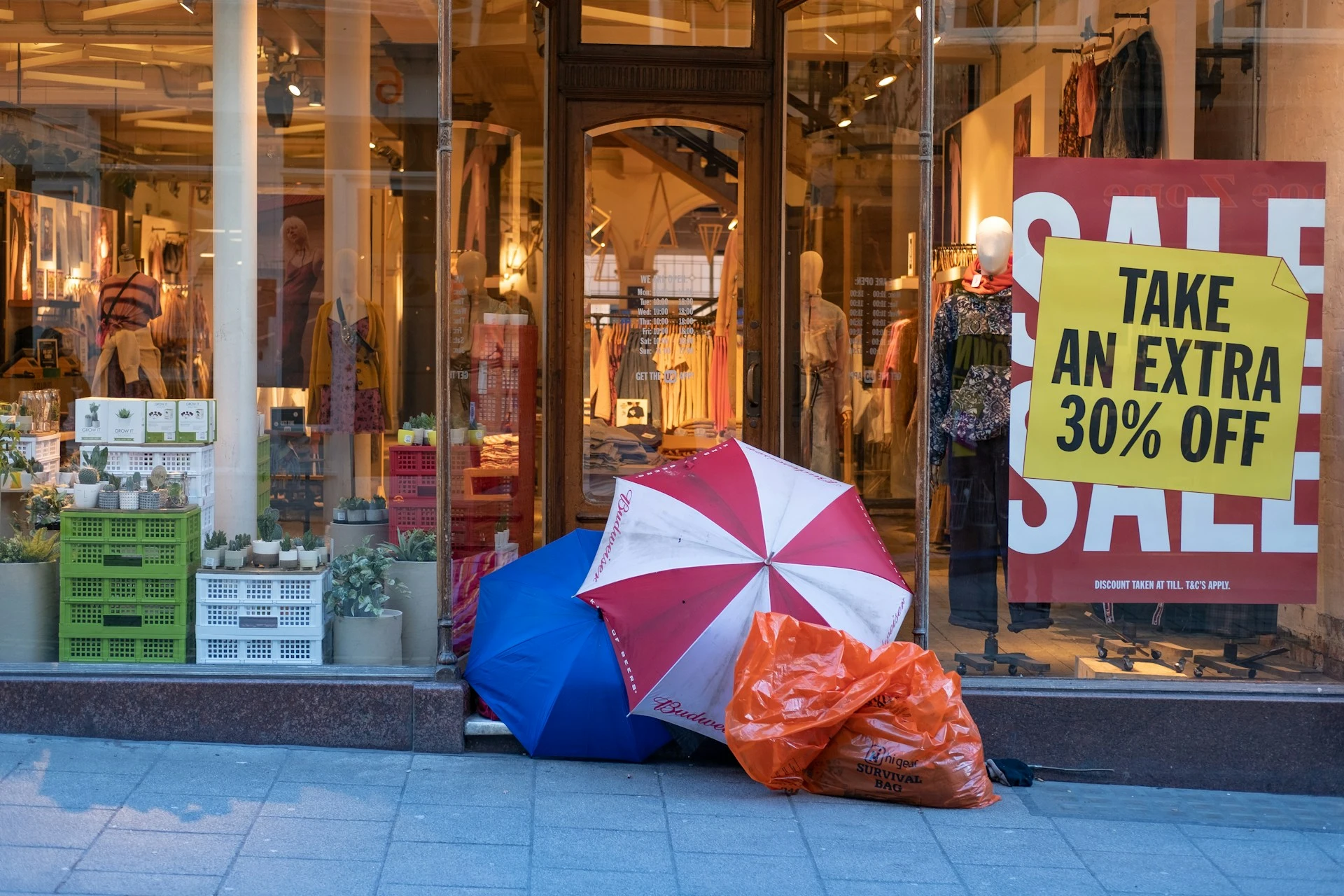 Eine Glasfassade eines Ladens mit SALE-Werbung, davor 2 bunte Regenschirme