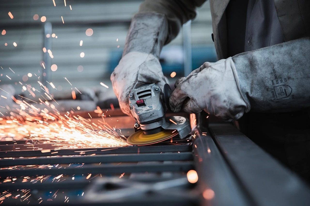 zwei Hände mit Schutzhandschuhen schweißen Metall, es fliegen Funken