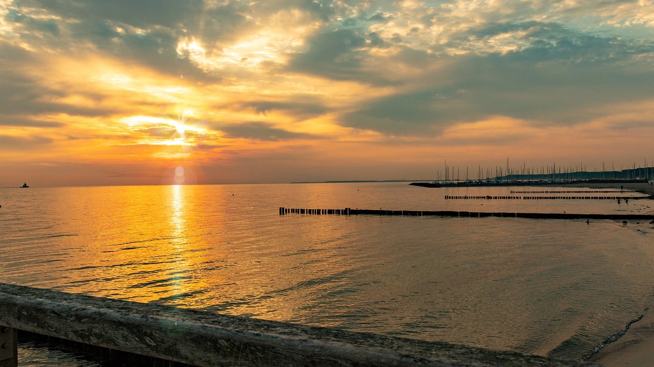 Sonnenuntergang an der Ostsee, im Hintergrund ein Segelhafen