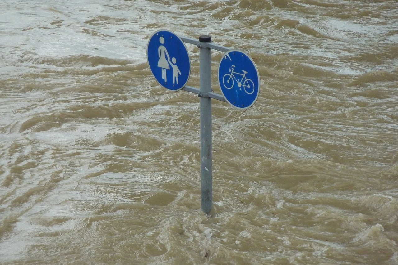 Das Foto zeigt eine überflutete Gegend. Aus dem Wasser ragt ein Schild für einen Rad- und Rußweg.