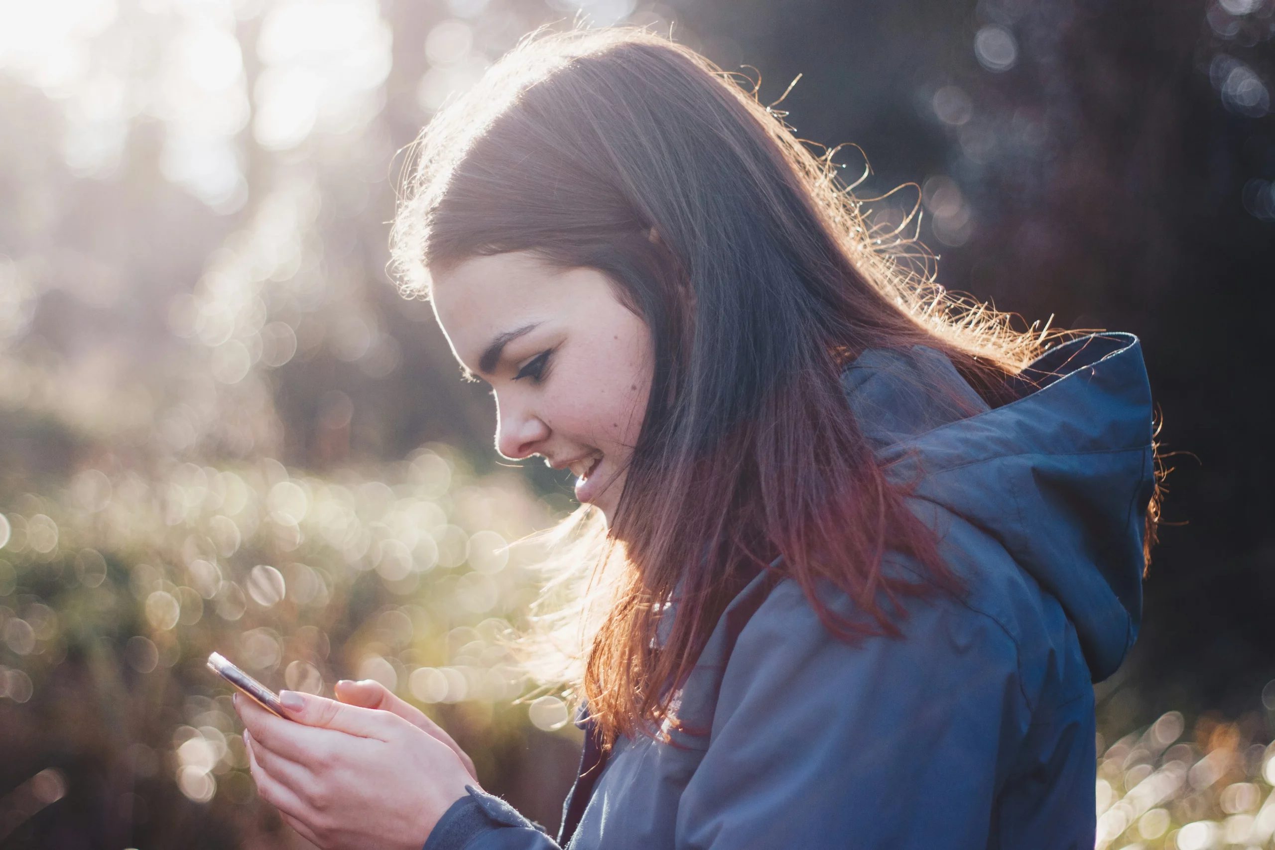 Eine junge Wanderin im Wald schaut begeistert auf ihr Handy