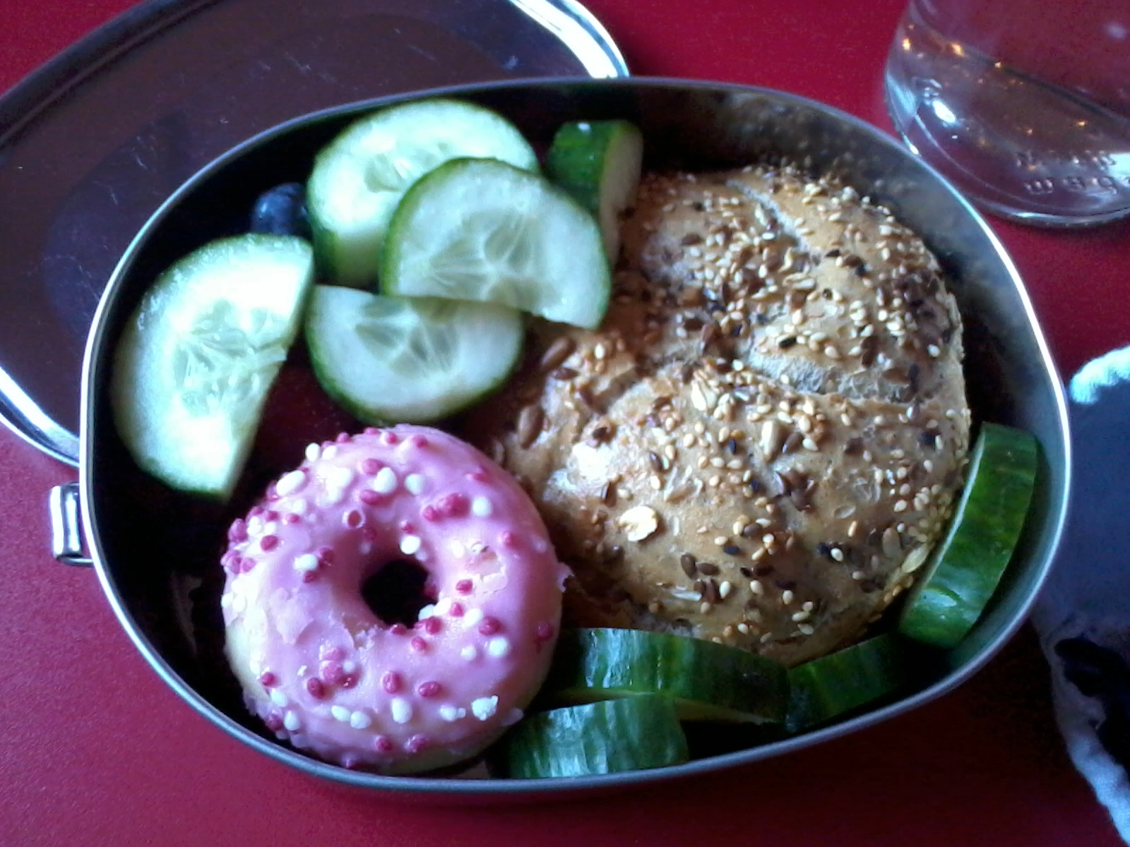 Das Foto zeigt eine gefüllte Edelstahlbox mit Brötchen, Donut, Gurken.