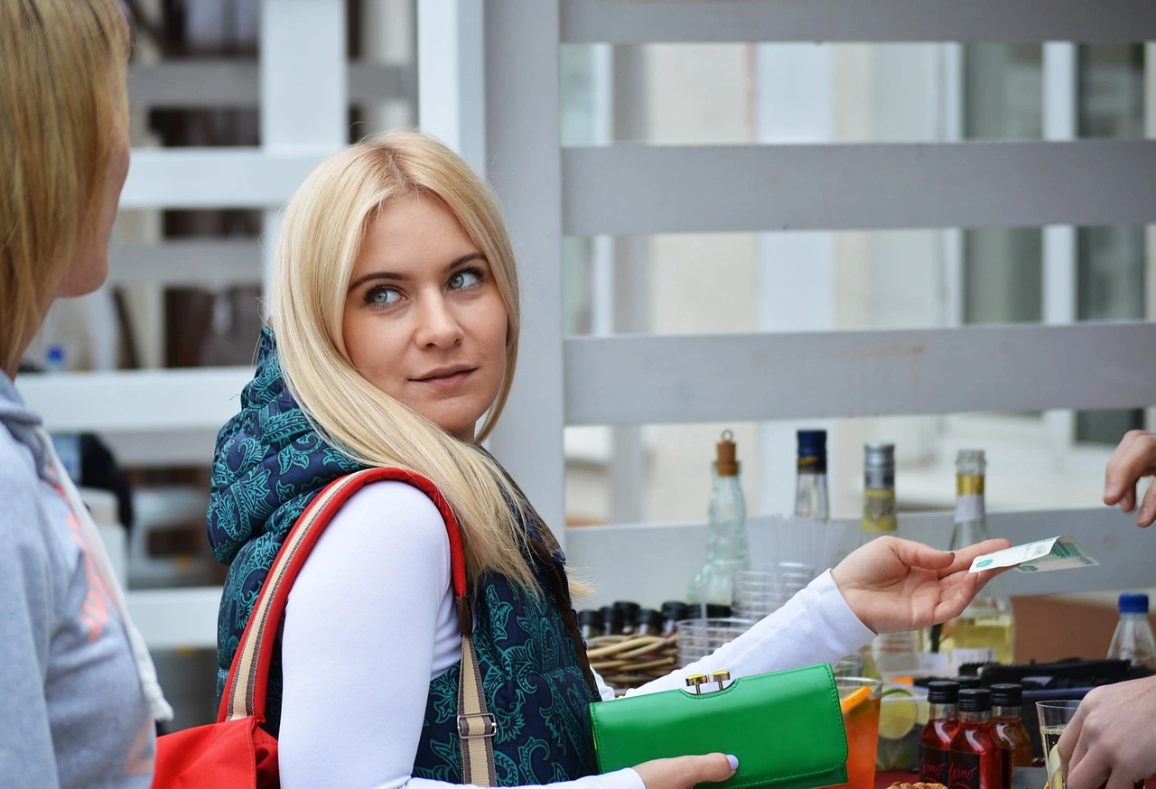 Das Foto zeigt eine Frau mit blonden, langen Haaren. Sie bezahlt gerade Ware.