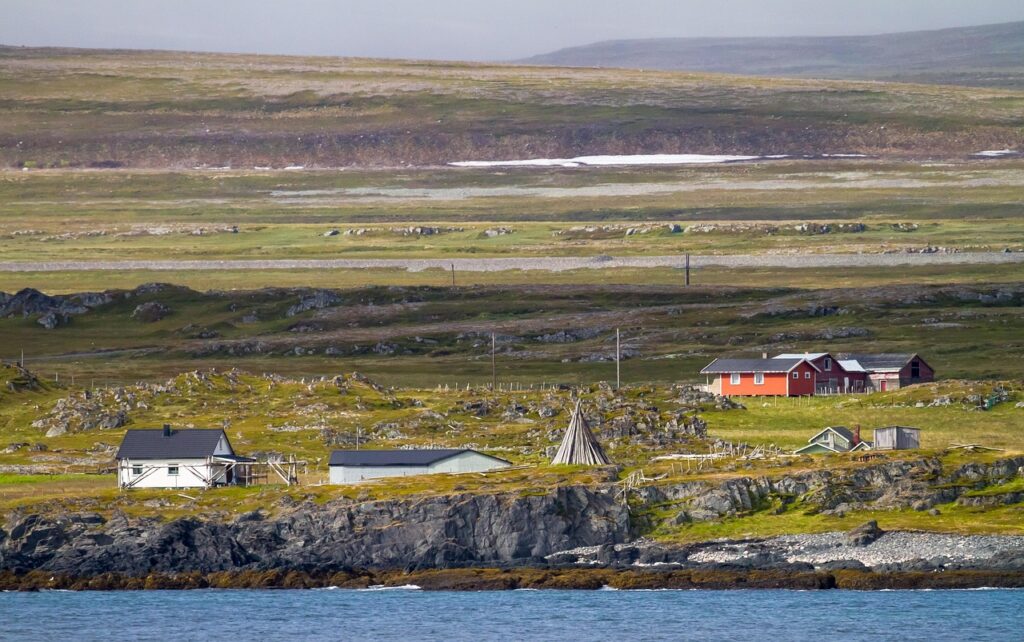 Mehrere niedrige Häuser an einer Steinküste, dahinter karge Tundra