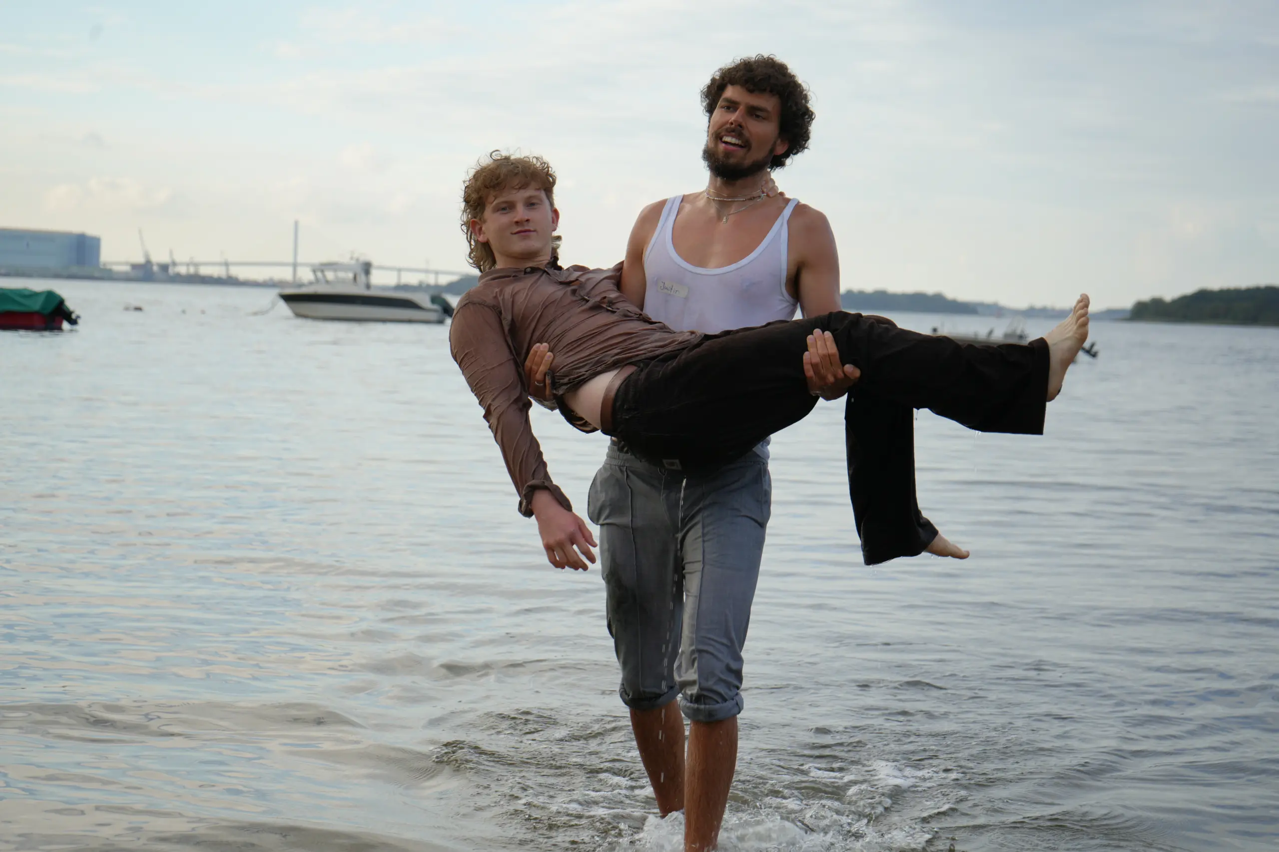 Justin steht bis zu den Knöcheln im Wasser und trägt Marvin wie eine Prinzessin auf dem Arm. Die beiden sind offensichtlich sehr nass vom Toben in der Ostsee.