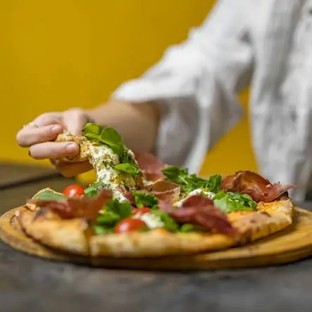 Eine Person, die sich ein Stück von einer Pizza schnappt
