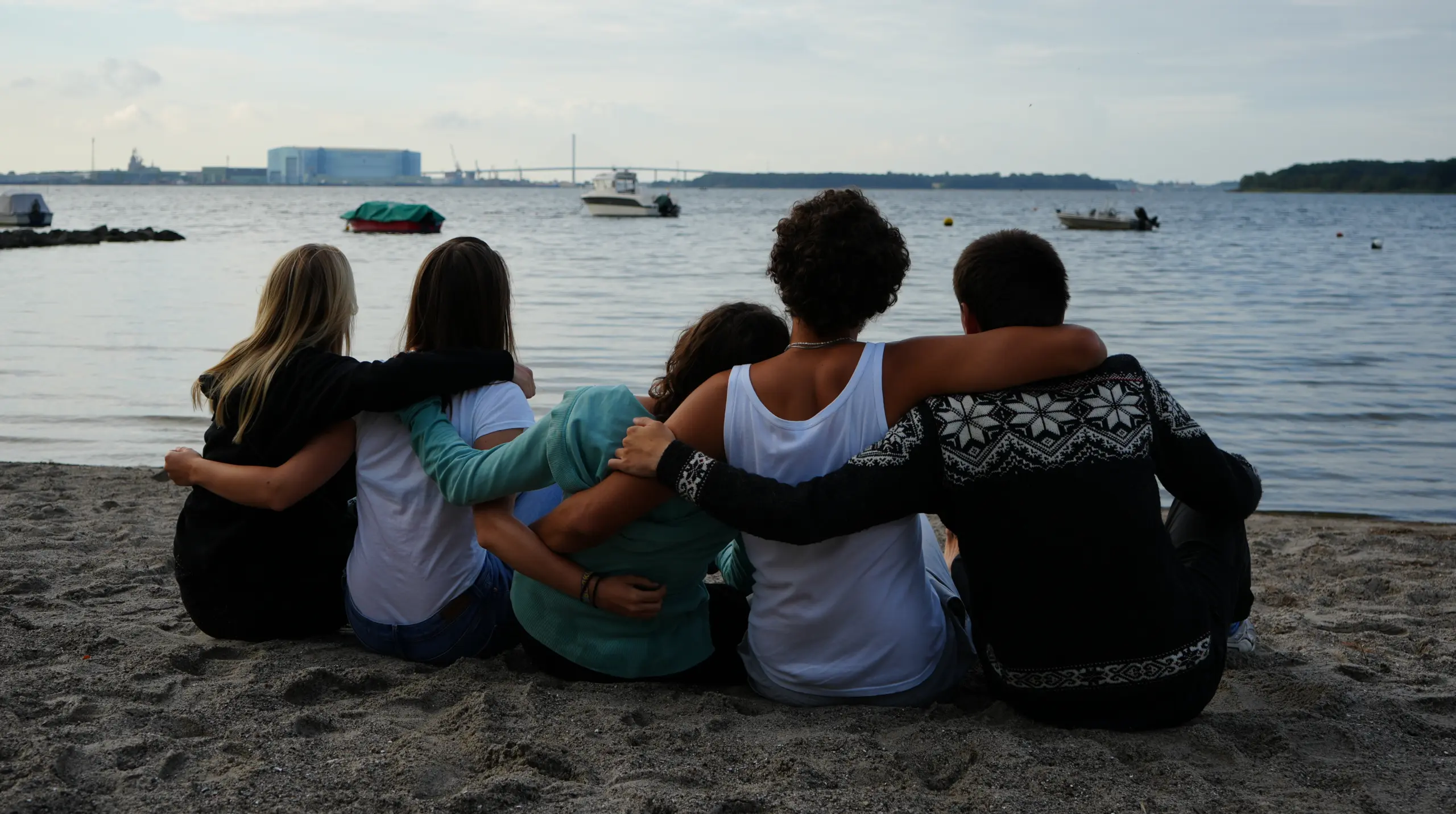 Eine Gruppe von fünf Menschen sitzt mit dem Rücken zum Bild am Strand und blickt über die Ostsee.