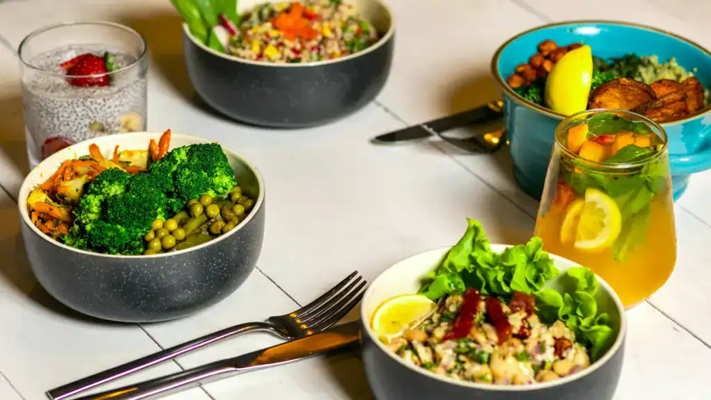 Tisch mit 4 unterschiedlich gefüllten Lunchboxen, Besteck und einem Getränk