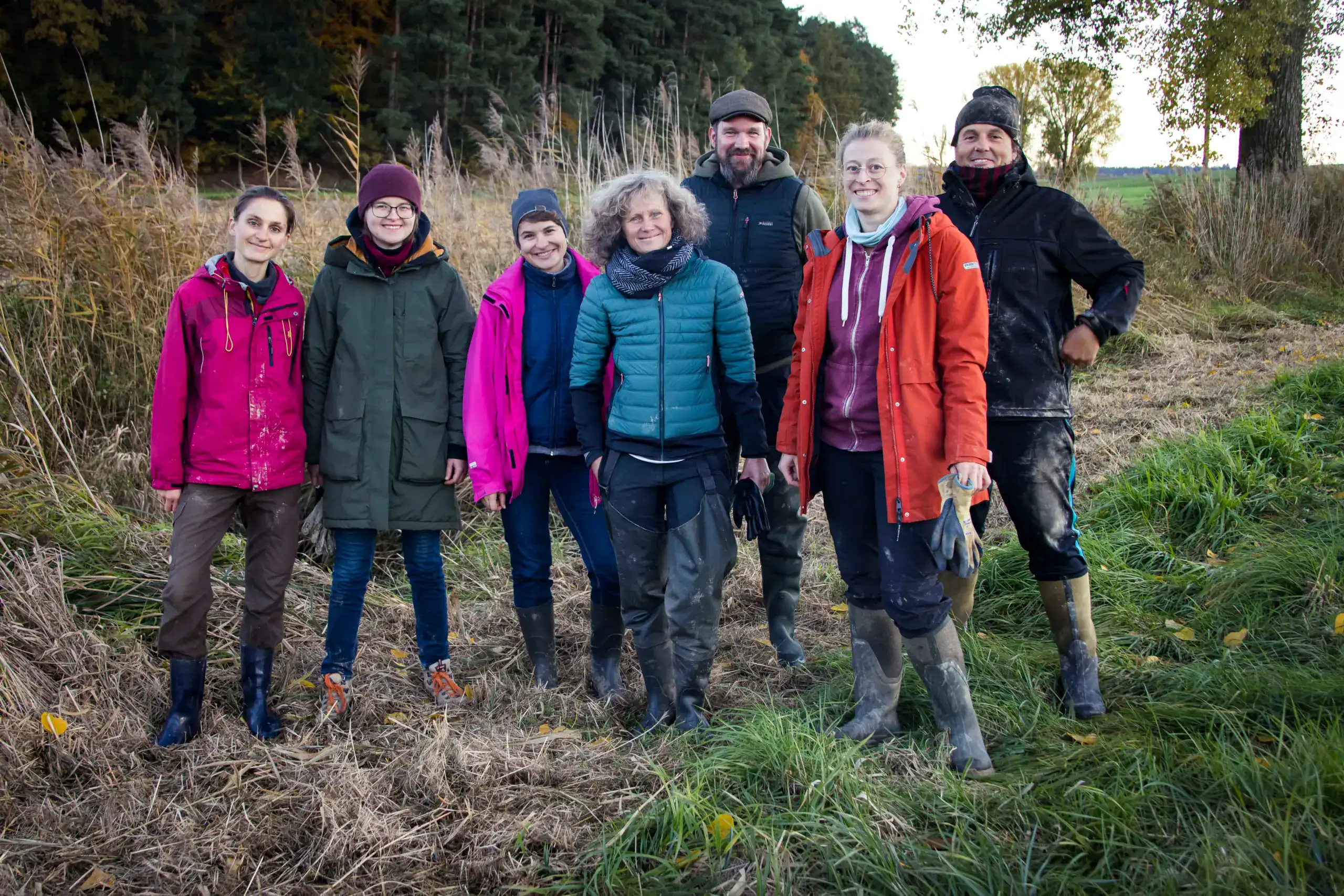 Eine Gruppe von 7 Menschen steht mit Gummistiefeln und Arbeitshandschuhen auf einer Wiese, im Hintergrund Bäume