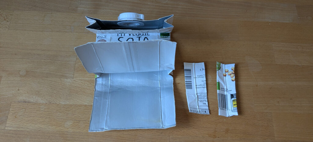 Das Tetrapak hat nun zwei voneinander unabhängige Laschen. Rechts daneben liegen die herausgeschnittenen Rechtecke.