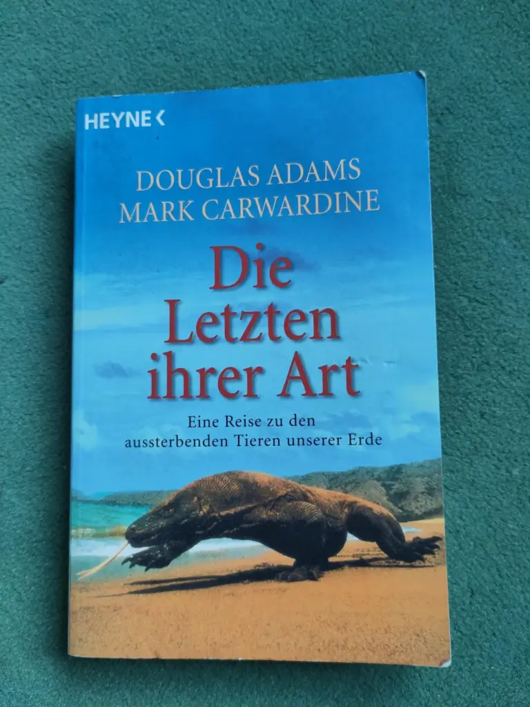 Das Bild zeigt das Cover des Buchs "Die letzten ihrer Art - Eine Reise zu den aussterbenden Tieren unserer Erde" von Douglas Adams und Mark Carwardine. Auf dem Cover ist ein Komodowaran am Strand abgebildet.