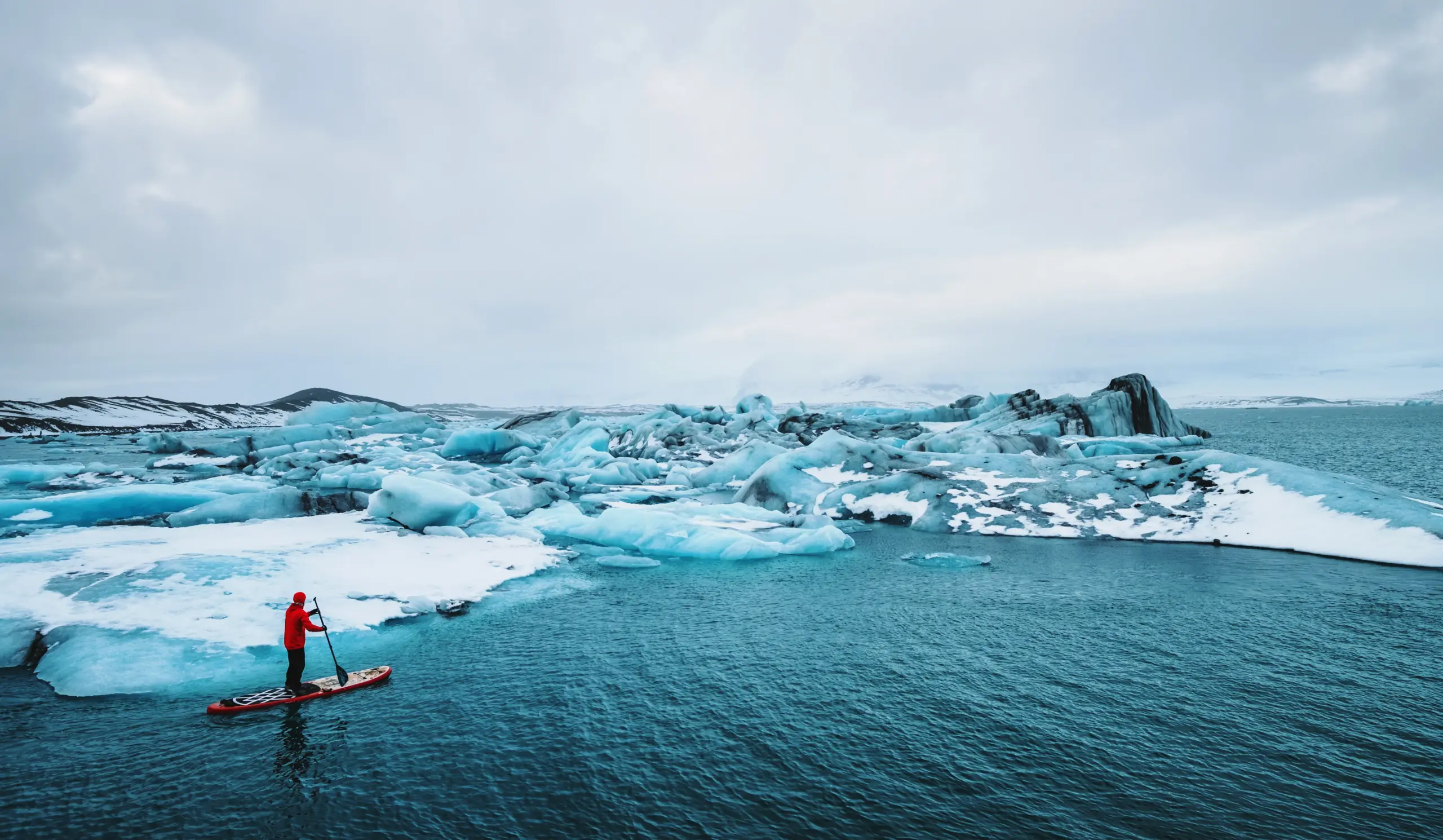 Eine Person macht Stand-Up Paddling in einer Eislandschaft.