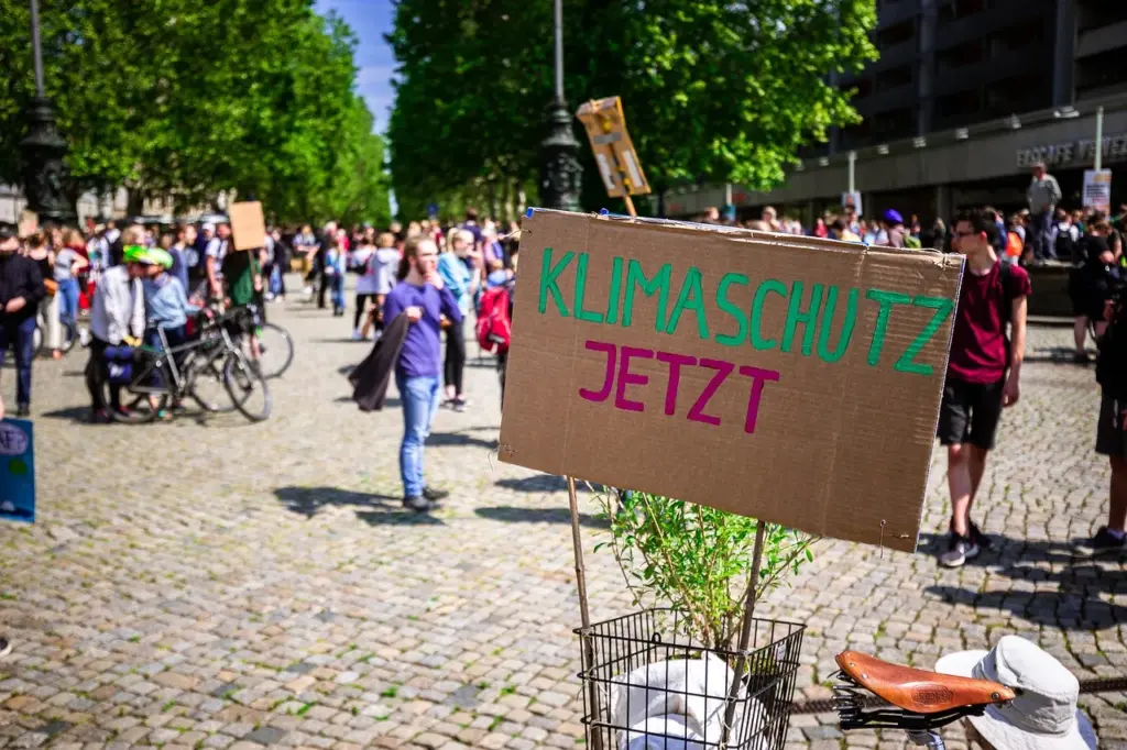 ein Schild mit der Aufschrift "Klimaschutz jetzt" steht vor einer Menschenmenge auf einem Platz