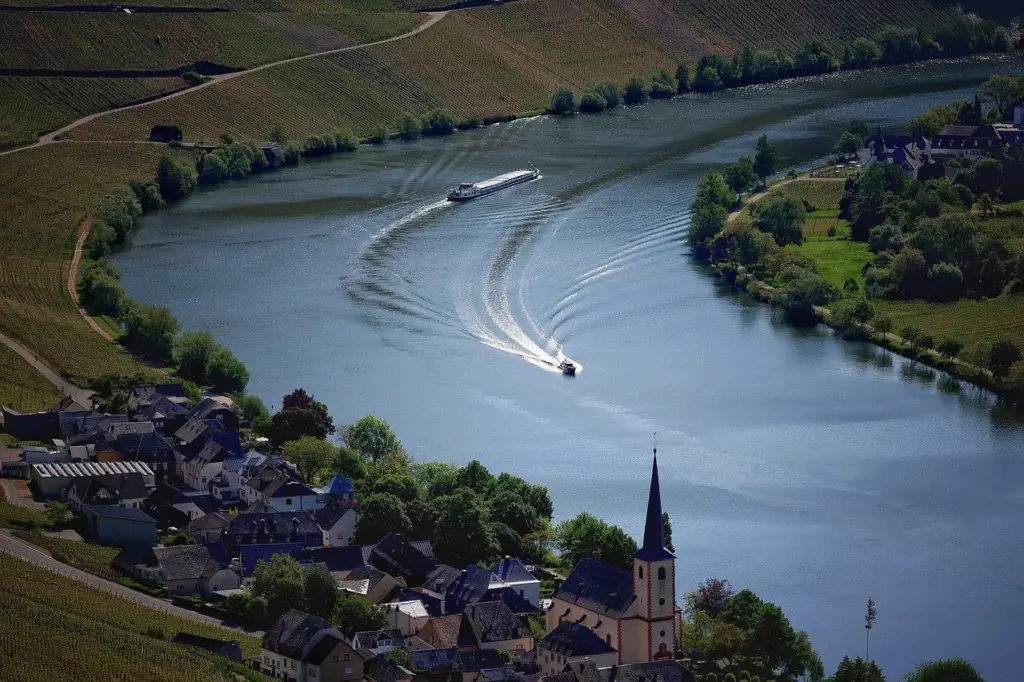 ein begradigter Fluss fließt durch landwirtschaftliche Flächen und ein Dorf, auf dem Fluss sind zwei Schiffe zu sehen