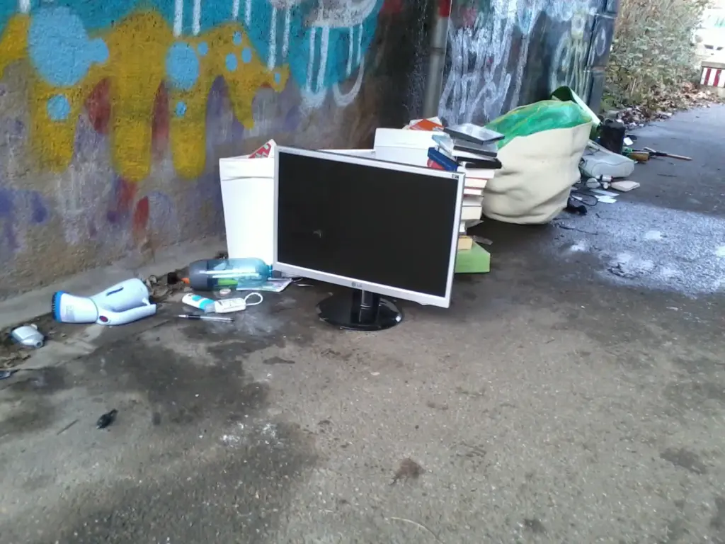 ein Haufen Müll steht unter einer Füßgängerbrücke, darunter ein PC-Bildschirm, ein Stapel Bücher sowie mehrere gefüllte Taschen