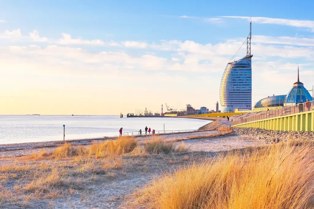 Blick auf Dünengras und Strand, im Hintergrund ein Hochhaus und futuristische Gebäude