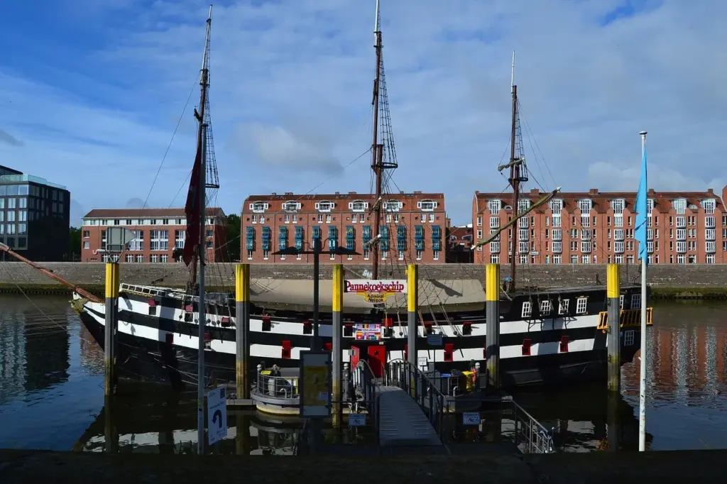 ein Schiff mit drei Masten liegt an einer Anlegestelle der Weser, im Hintergrund rötliche Häuser