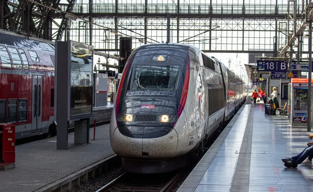 ein rot-weißer Zug der SNCF steht auf einem Bahngleis, daneben ein roter Regionalzug