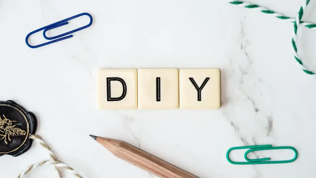 Drei Scrabblesteine bilden das Wort "DIY", darum einige Büroklammern, ein Bleistift und Schnüre