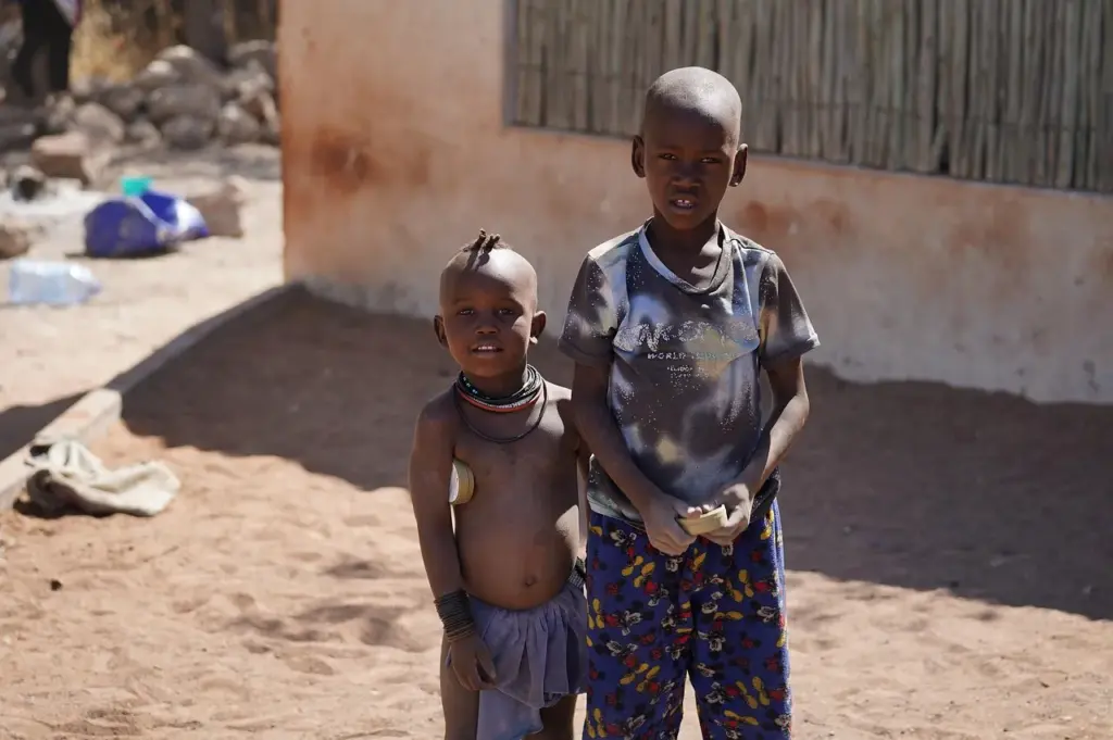 zwei Kinder stehenvor einer Hütte in einem afrikanischen Land, der Boden ist trocken und staubig