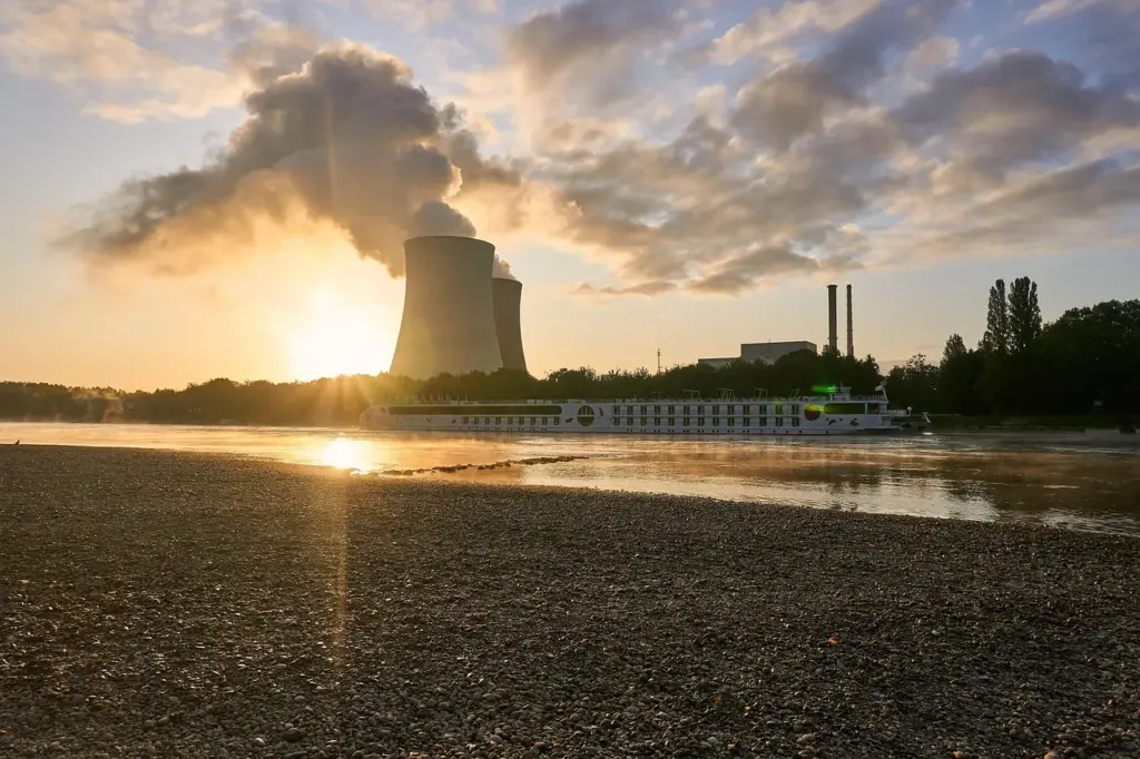 ein Fluss führt Niedrigwasser, im Hintergrund die Türme eines Atomkraftwerkes in der Abendsonne