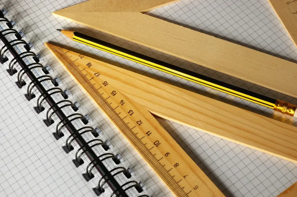 zwei Lineale aus Holz und ein Bleistift liegen auf einem karierten Block