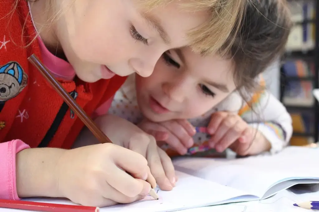 zwei jüngere Mädchen beugen sich über ein Heft und schreiben