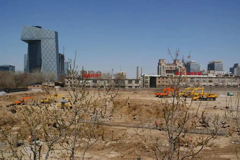 Blick auf eine Baustelle mit mehreren Baustellenfahrzeugen, im Hintergrund mehrere Gebäude