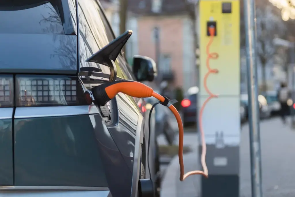 eine graues Elektro-Auto steht an einer gelben Ladesäule und ist mit dem Ladekabel verbunden