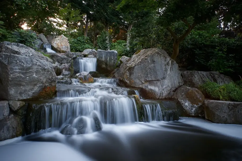 ein Wasserfall fließt zwischen größeren Steinen, im Hintergrund Bäume