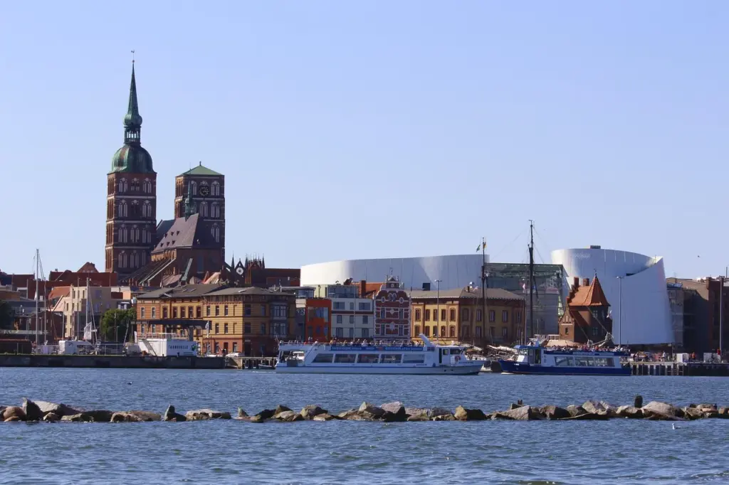 Blick vom Strealsund aus auf Stralsund, zwei Kirchtürme, mehrere Backsteinhäuser sowie das große weiße Gebäude des Ozeaneums sind zu sehen, im Vordergrund Wasser und Schiffe