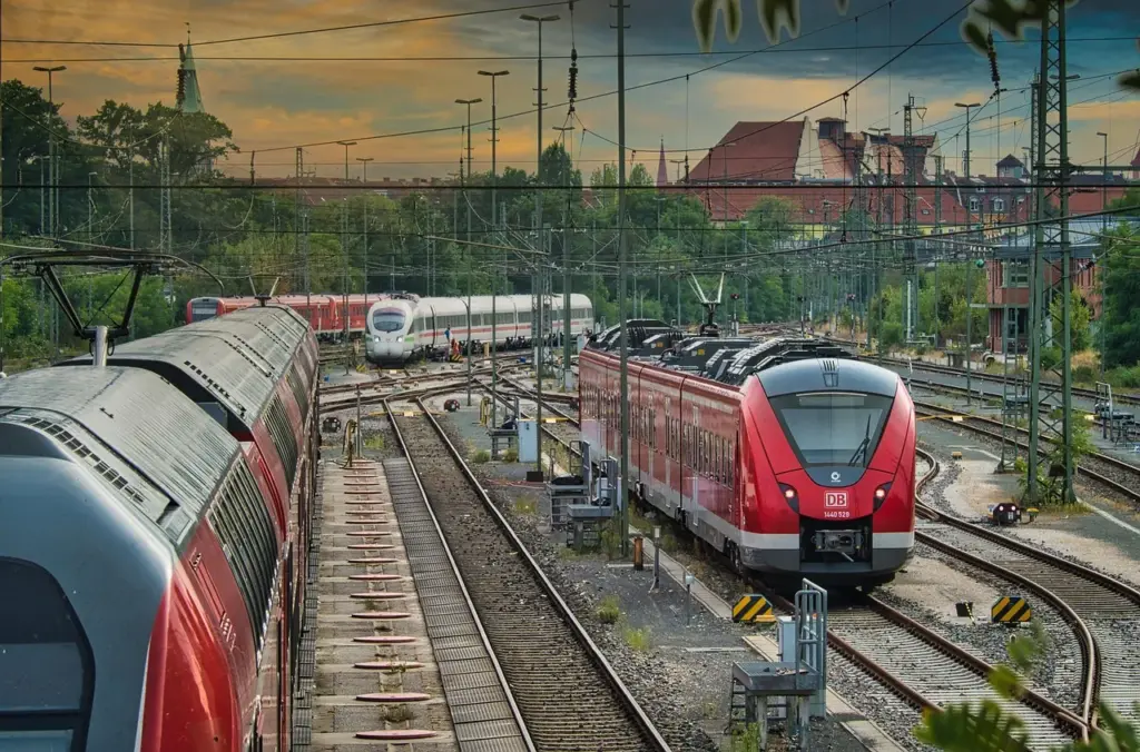 mehrere Gleise nebeneinander, auf denen 3 rote Regionalbahnen und im Hintergrund ein weißter ICE stehen