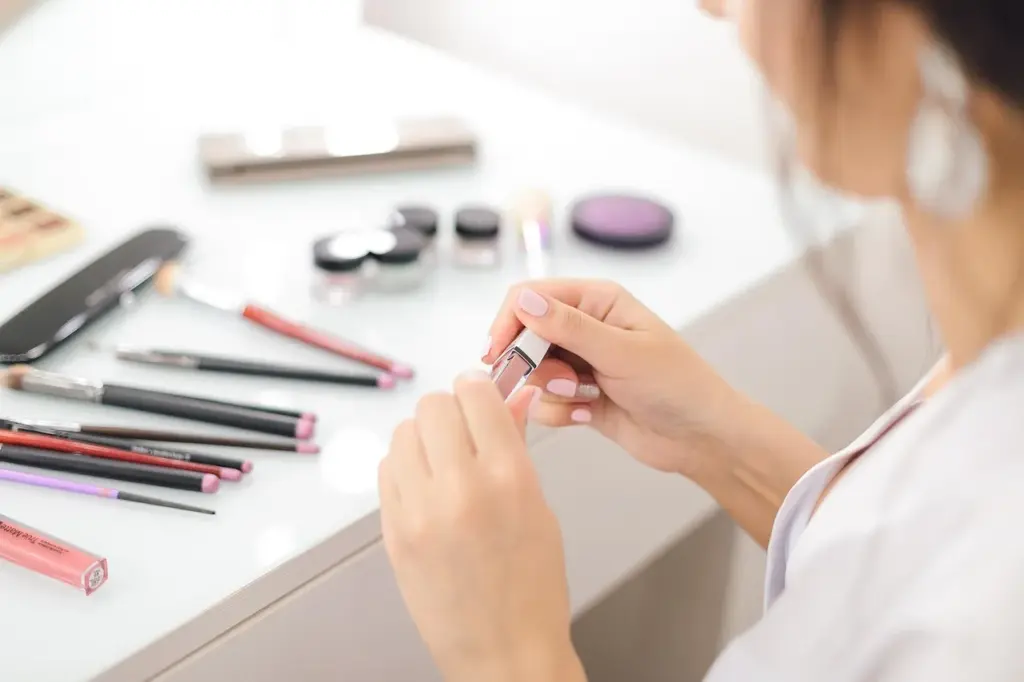 verschiedene Schminkutensilien liegen vor einer weiblichen Person, sie hält ein Fläschchen Nagellack in den Händen